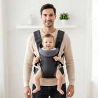 SMOVO Hug Babytrage – Vater mit Baby in dunkelgrauer 
strukturierter Trage, helles minimalistisches Zimmer